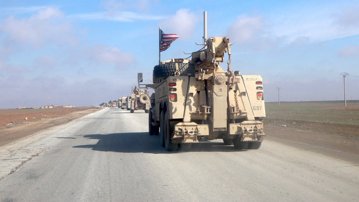 Armored U.S. military vehicles accompany a convoy of passenger buses carrying detainees along a road from northeastern Syria into Iraq.