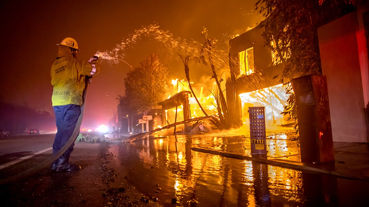 Firefighter holds hose with water coming out as fire burns
