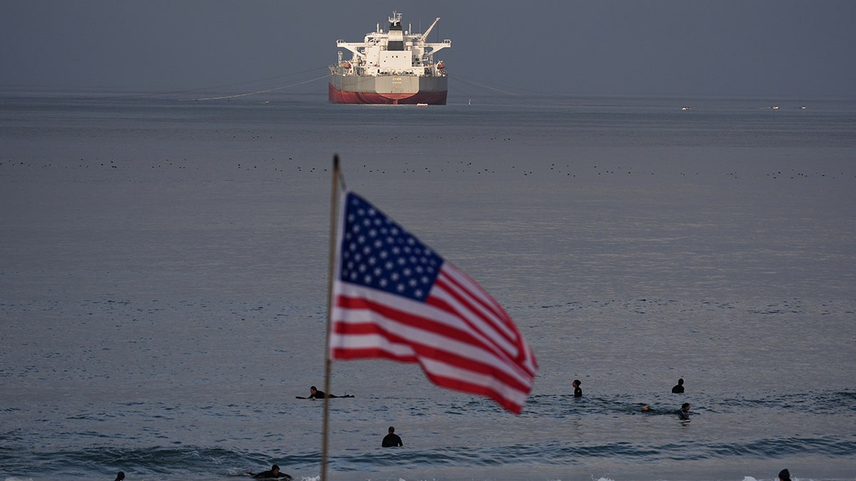 Surfers waiting for waves in the water at El Porto Beach near a large crude oil tanker.