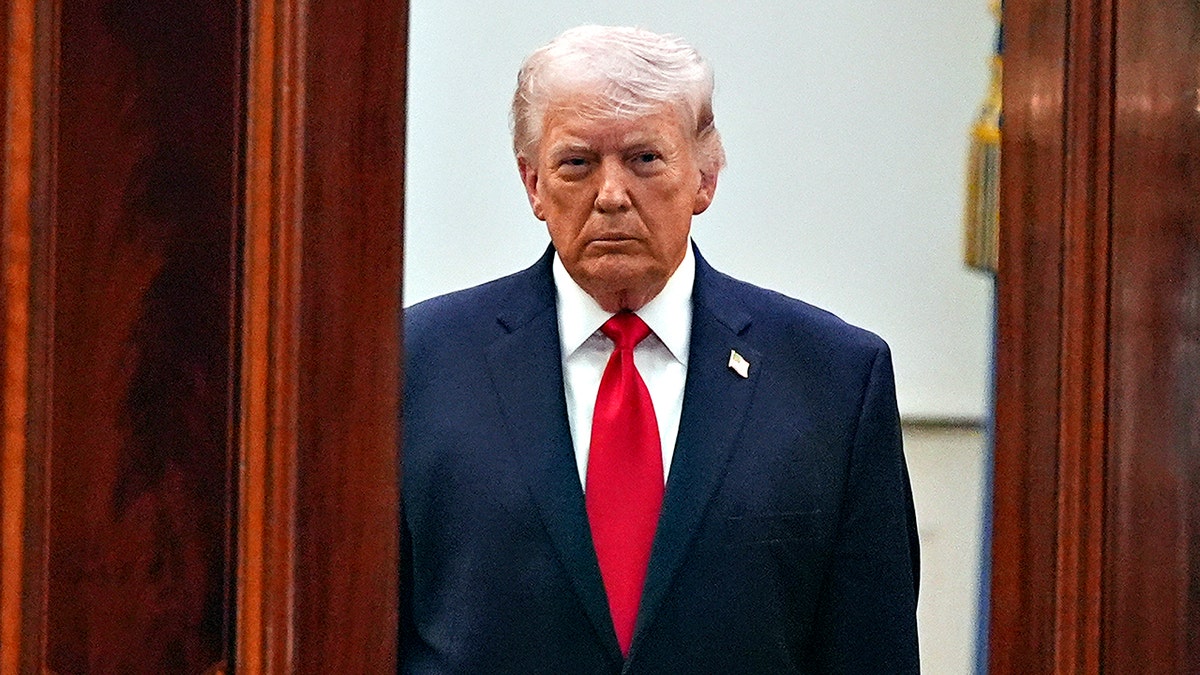 Donald Trump in dark suit and red tie looking ahead stern