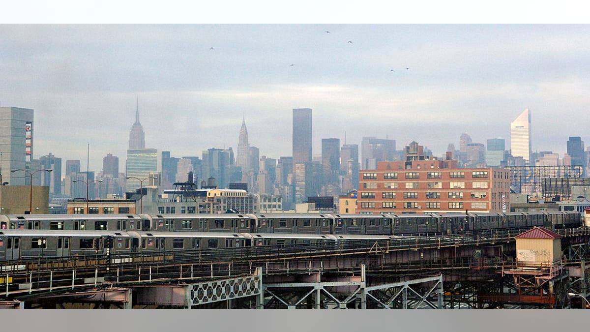 Queensboro Plaza subway station with trains arriving and departing and New York City skyline in background