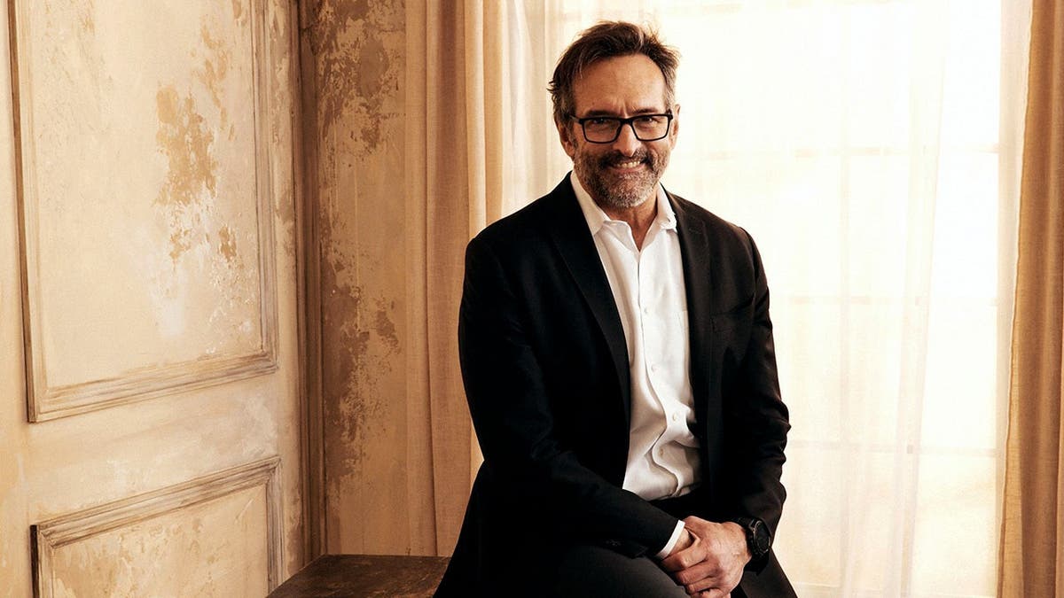Roger D. Carstens posing for a portrait in front of a blue and white backdrop.