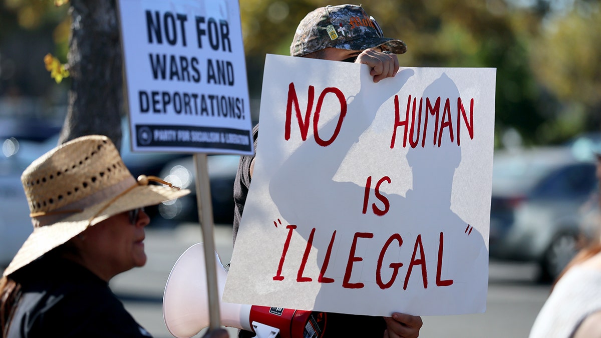 Protesters holding signs including one that reads No human is illegal at a demonstration