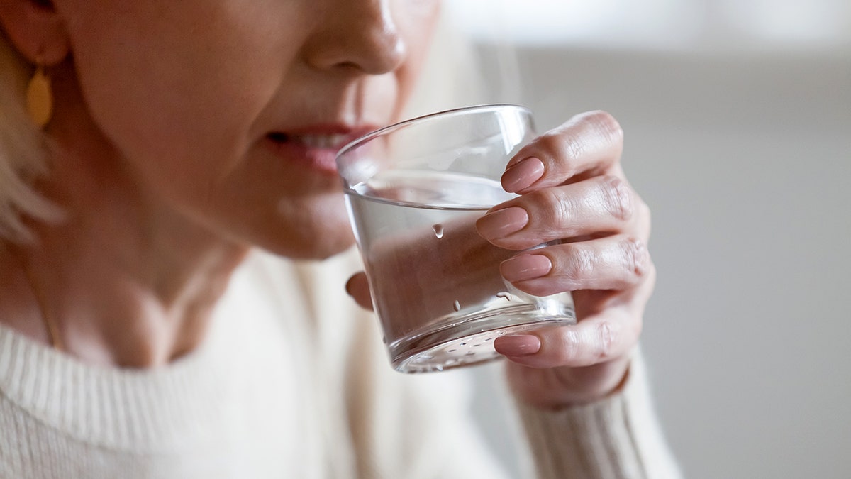Senior woman holding a glass of water and raising it to her lips