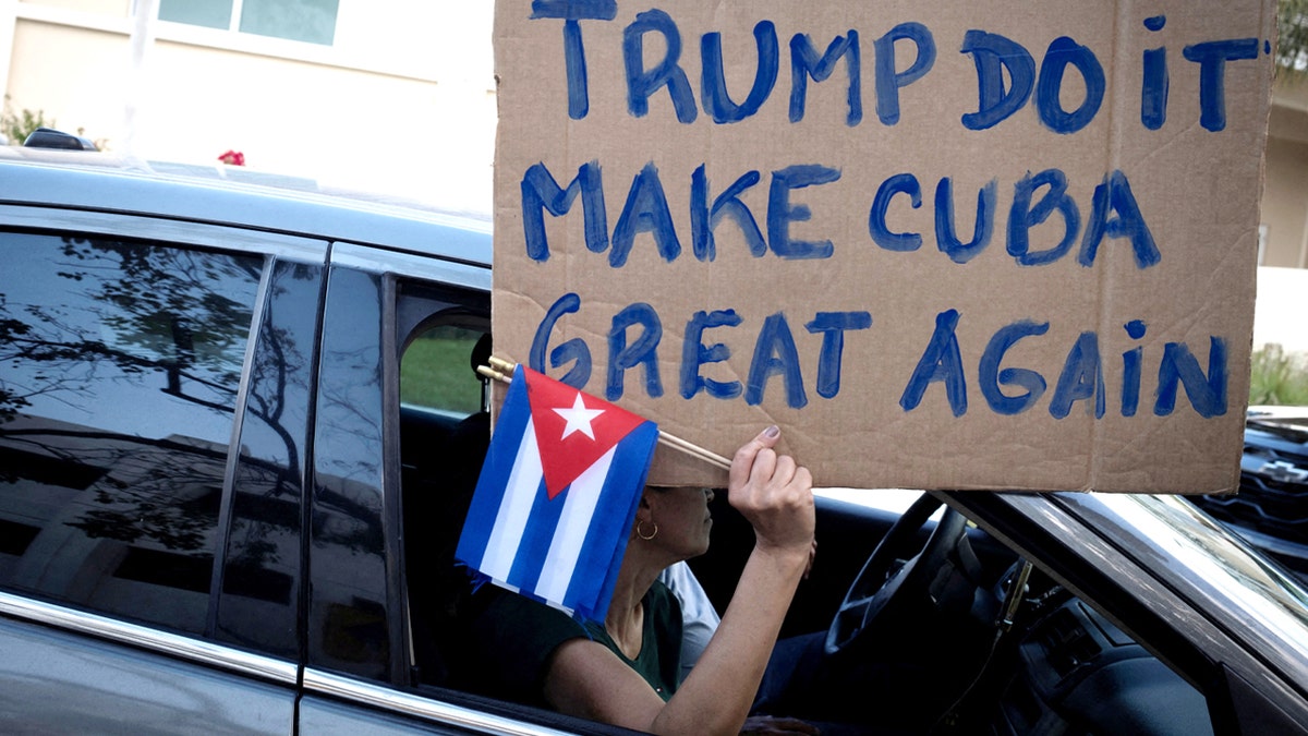 A woman holding a sign and Cuban flags at a protest in Miami