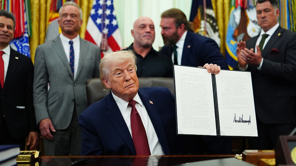 President Donald Trump holds up executive order he signed