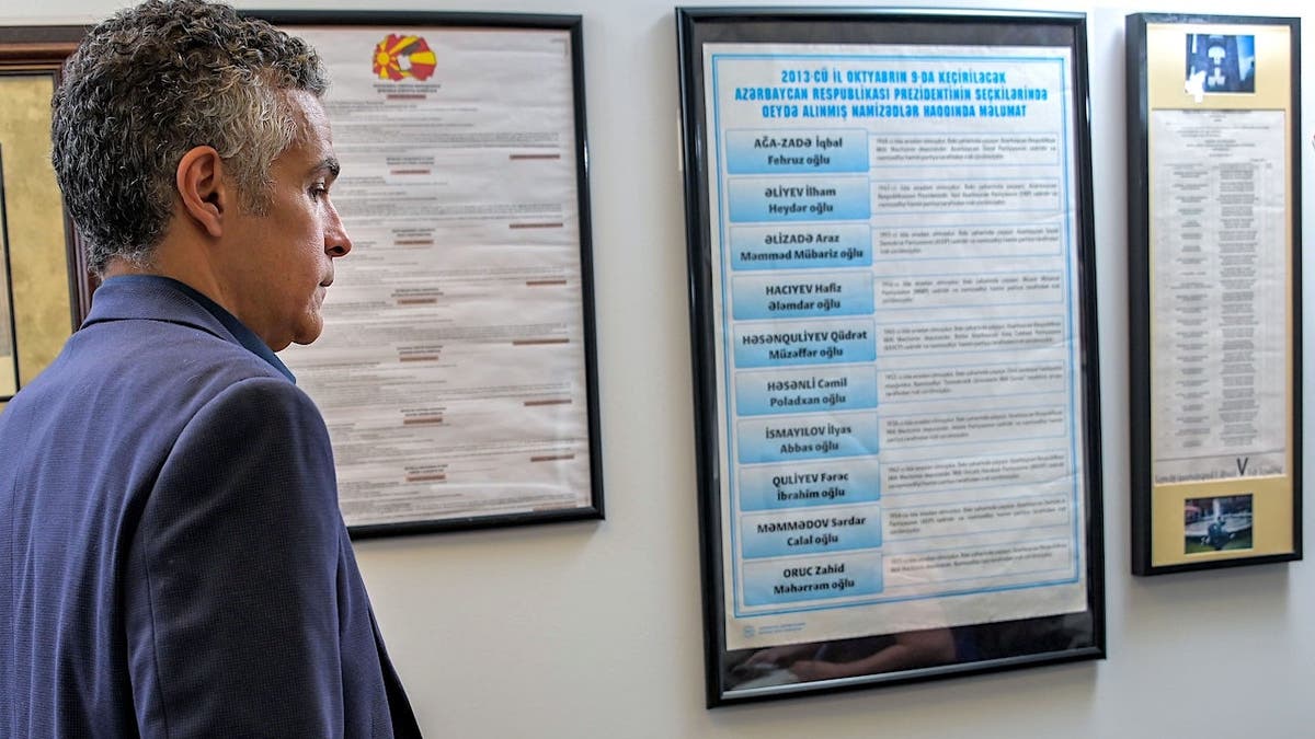 Jared DeMarinis standing in an office with sample ballots from North Macedonia, Azerbaijan and Armenia hanging on the wall