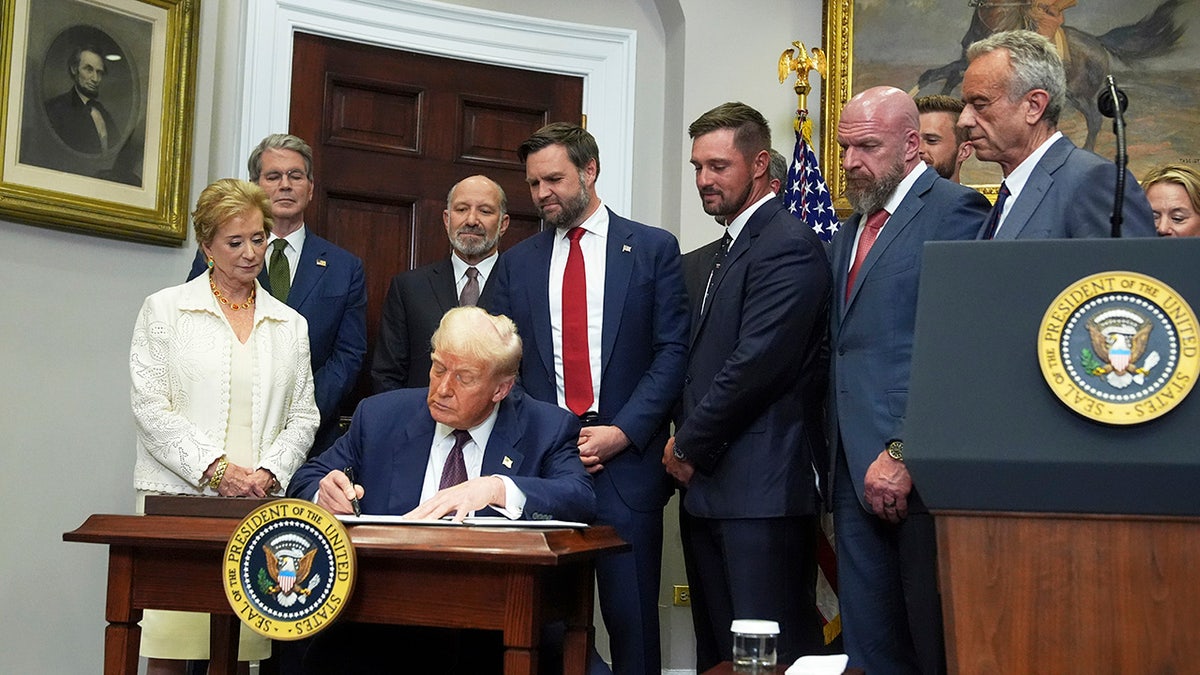 President Donald Trump signing an executive order in the Roosevelt Room with officials watching