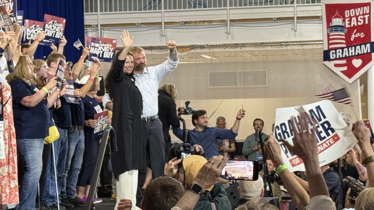 Graham Platner and wife waving on stage to supporters