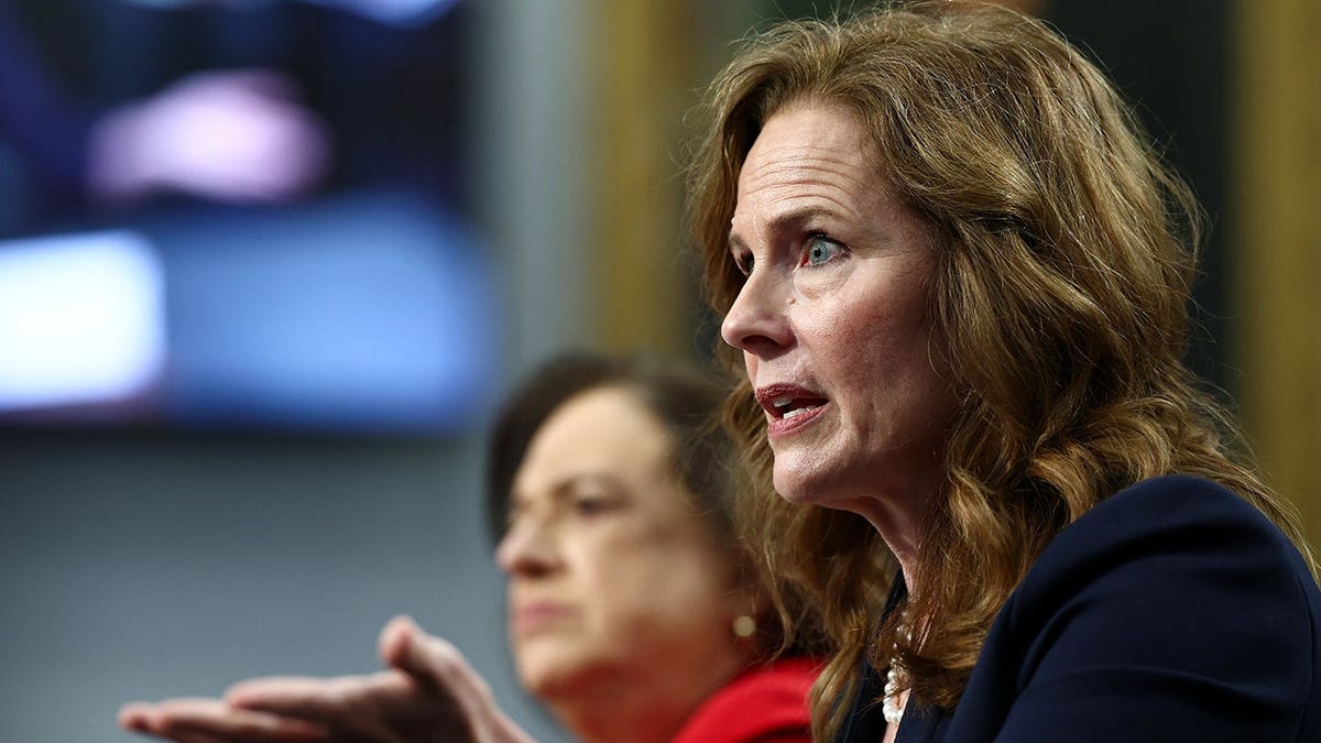 Elena Kagan and Amy Coney Barrett sitting at a table and testifying before a committee.x
