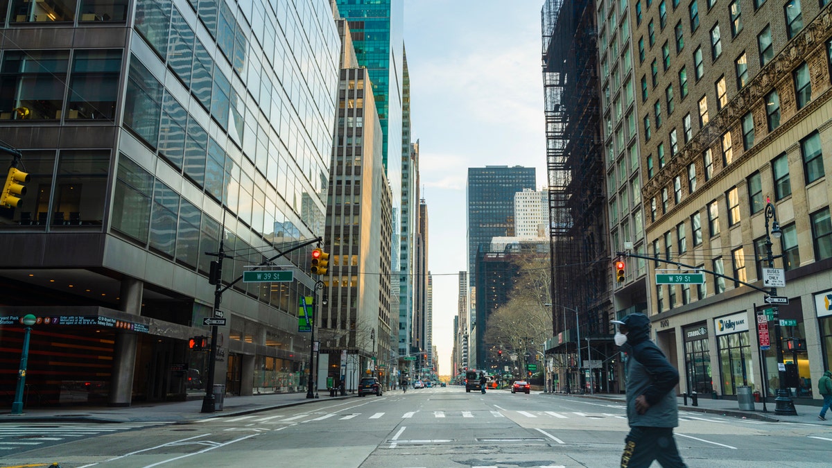 A black man wearing protective mask man crossing 6th Avenue of Americas in Midtown Manhattan deserted because of the city lockdown caused by COVID-19 pandemic.