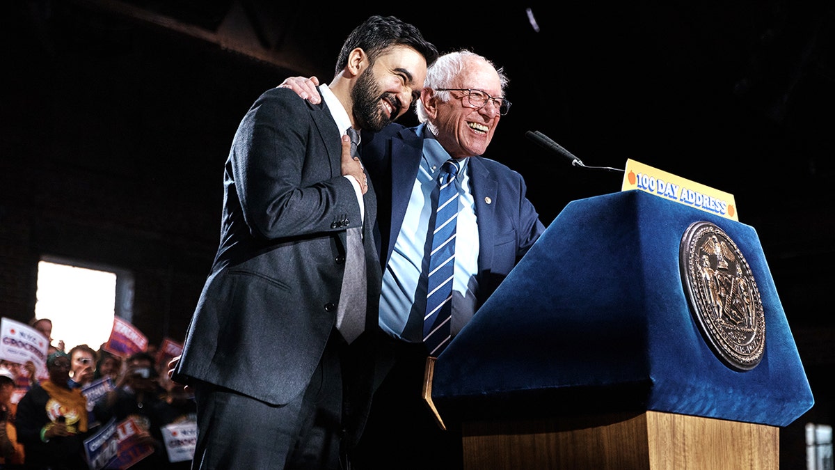 Zohran Mamdani and Bernie Sanders hugging on a stage.