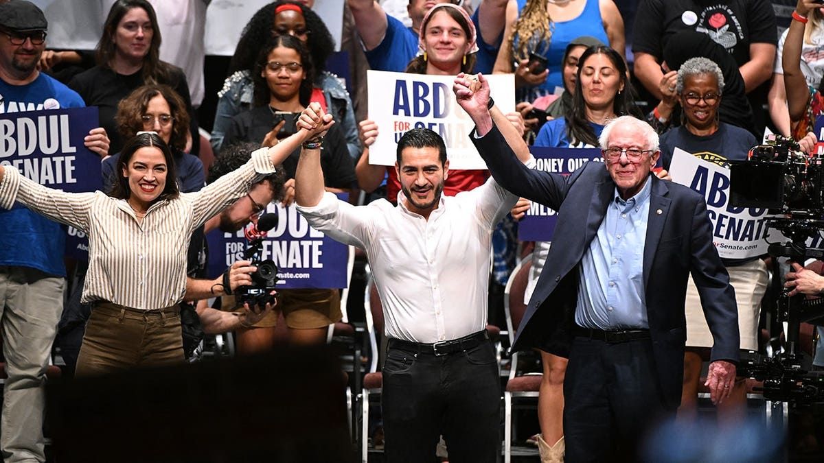 Alexandria Ocasio-Cortez, Abdul El-Sayed and Bernie Sanders join hands after a campaign rally.