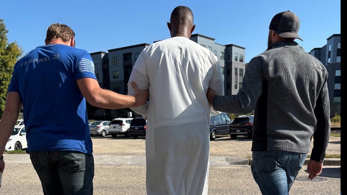 CIS officers walk alongside detained immigrant