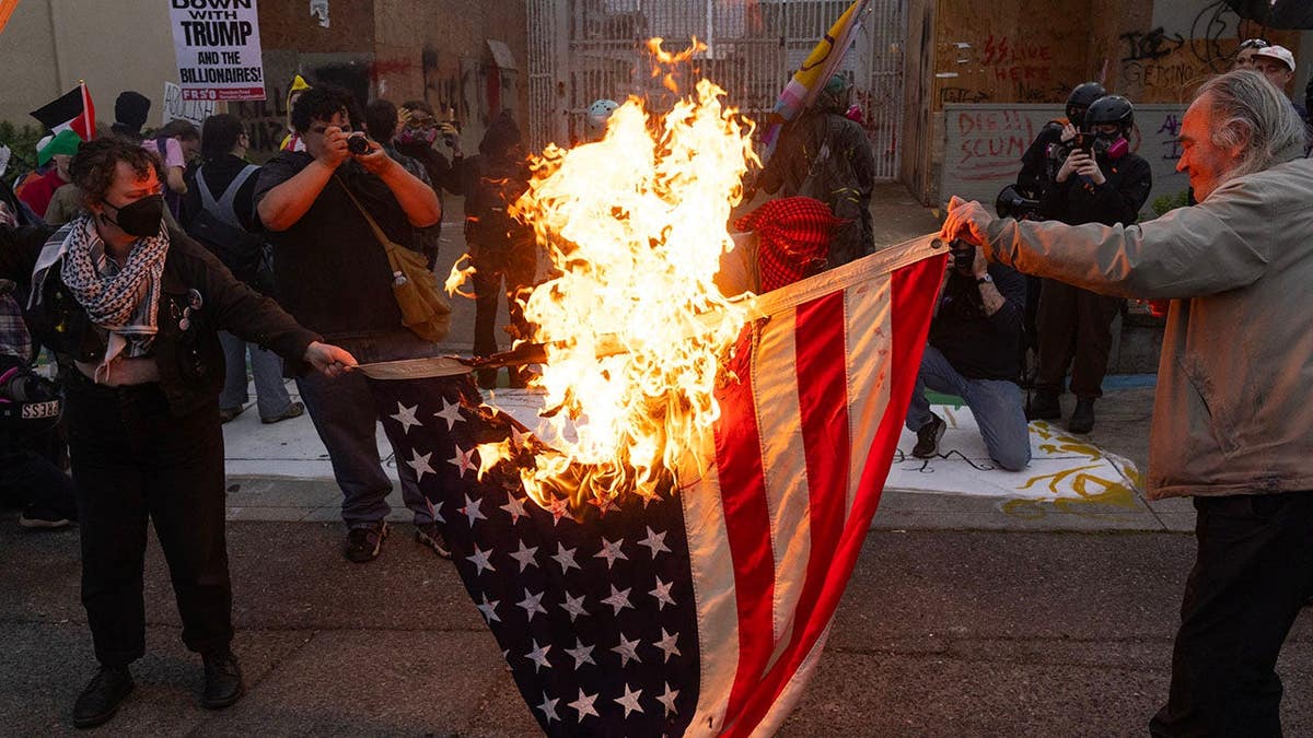 Demonstrators burn an American flag outside an ICE detention center in South Portland, Ore.