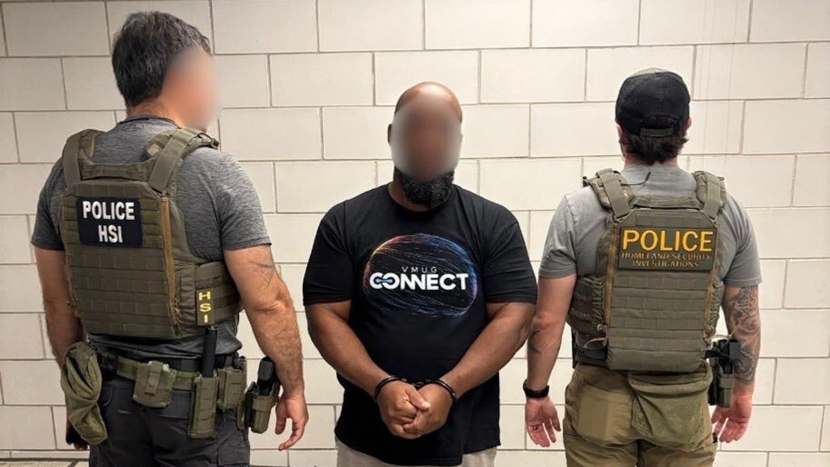 Officers with Homeland Security Investigations stand on either side of Alan Barbu Kargbo