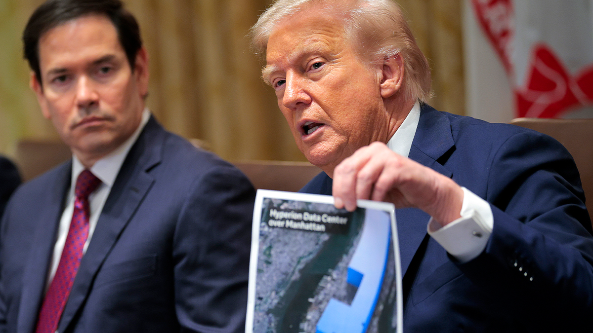Donald Trump sitting at a table holding up a picture of a data center during a meeting.