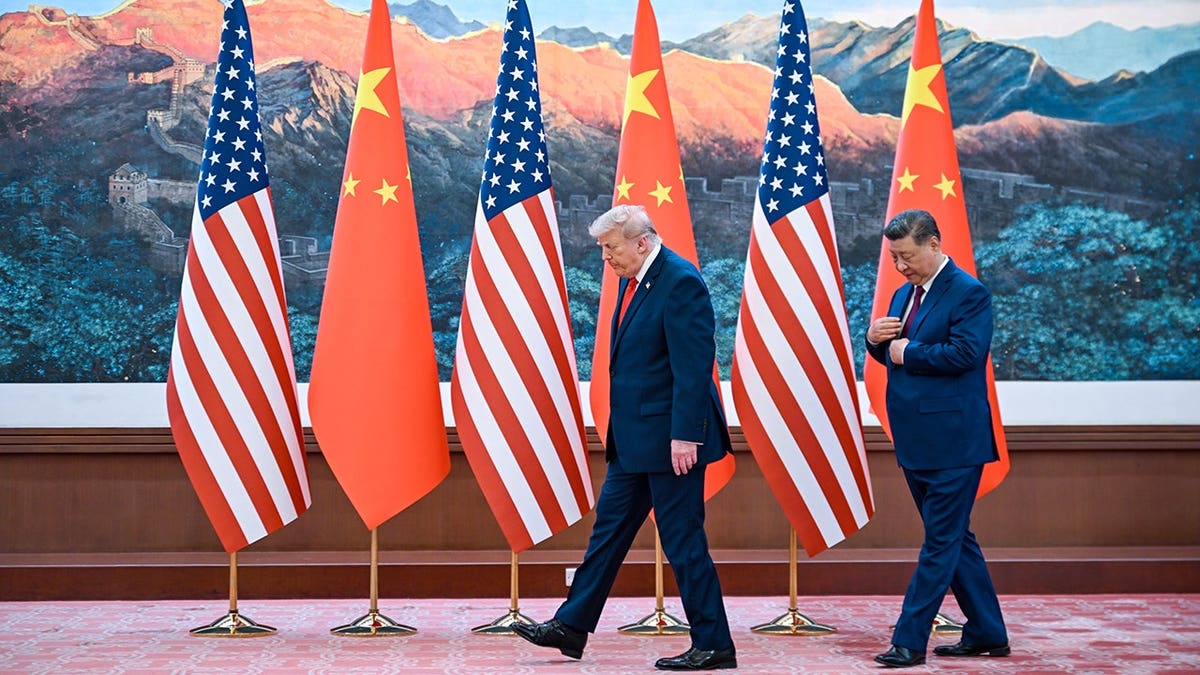 Donald Trump and Xi Jinping walk past a row of American and Chinese flags in front of a mural.