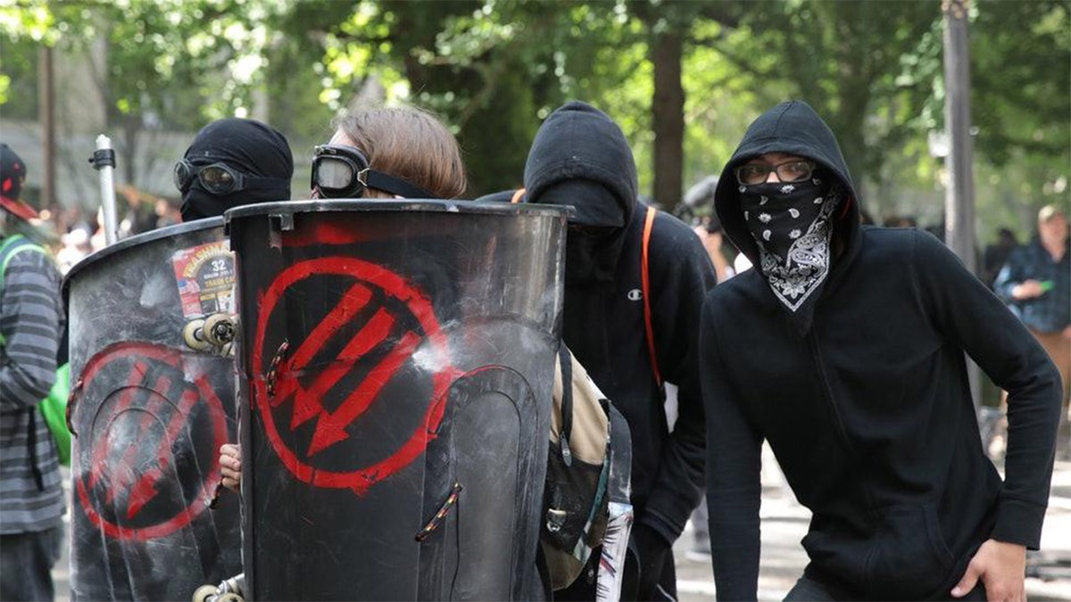 Antifa members in a riot with the three arrows symbol painted on their riot shields.