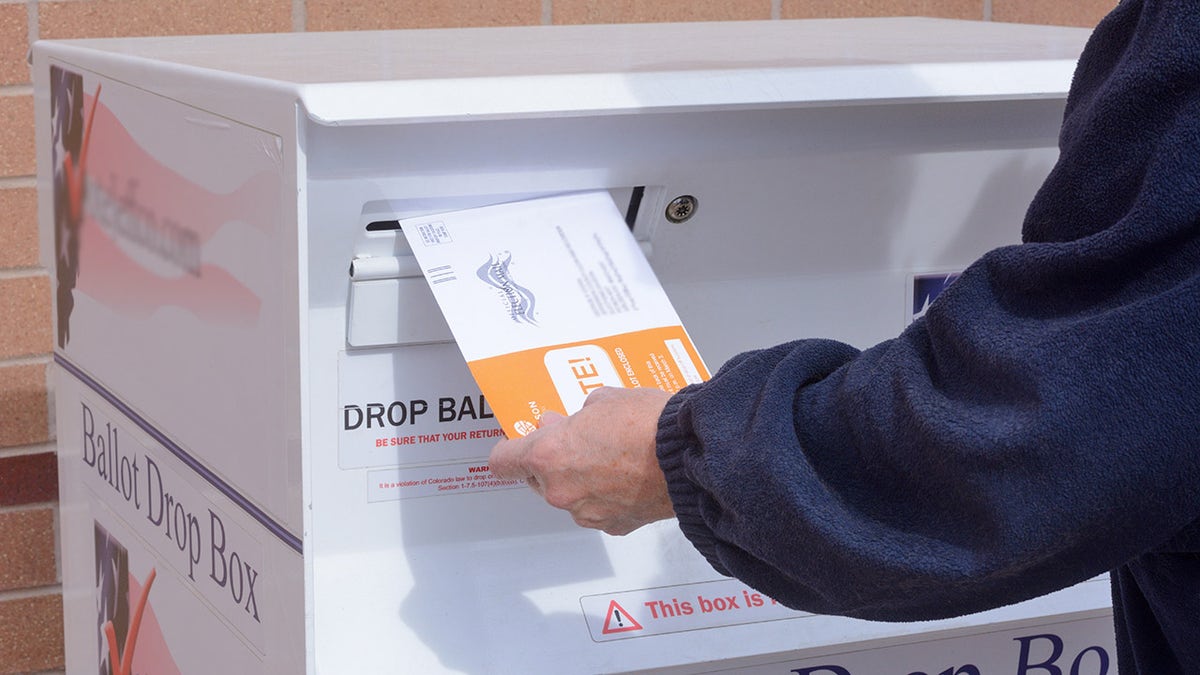 A person places a ballot envelope into a drop box during early voting.