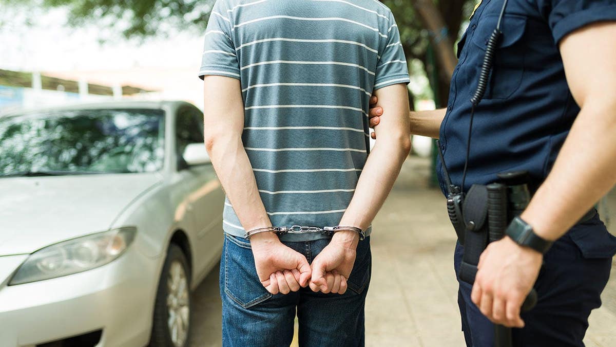 Handcuffed suspect stands with police officers during an arrest scene.