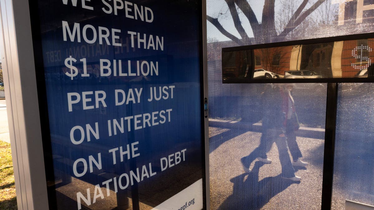 Two women walk past a bus stop where there is a National Debt Clock billboard display showing the United States gross national debt and each American family's share of the debt in Washington, DC, on December 30, 2024. The Congressional Budget Office has stated that the U.S. national debt is poised to top $56 trillion by 2034, as rising spending and interest expenses outpace tax revenues. The mounting costs of Social Security and Medicare continue to weigh on the nation's finances, along with rising interest rates, which have made it more costly for the federal government to borrow huge sums of money. (Photo by ROBERTO SCHMIDT / AFP) (Photo by ROBERTO SCHMIDT/AFP via Getty Images)