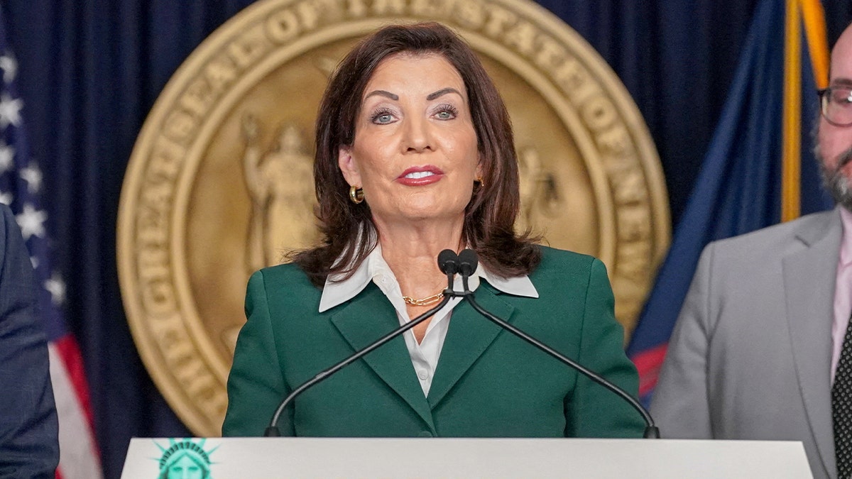 Kathy Hochul stands at a podium speaking to reporters during a press conference.