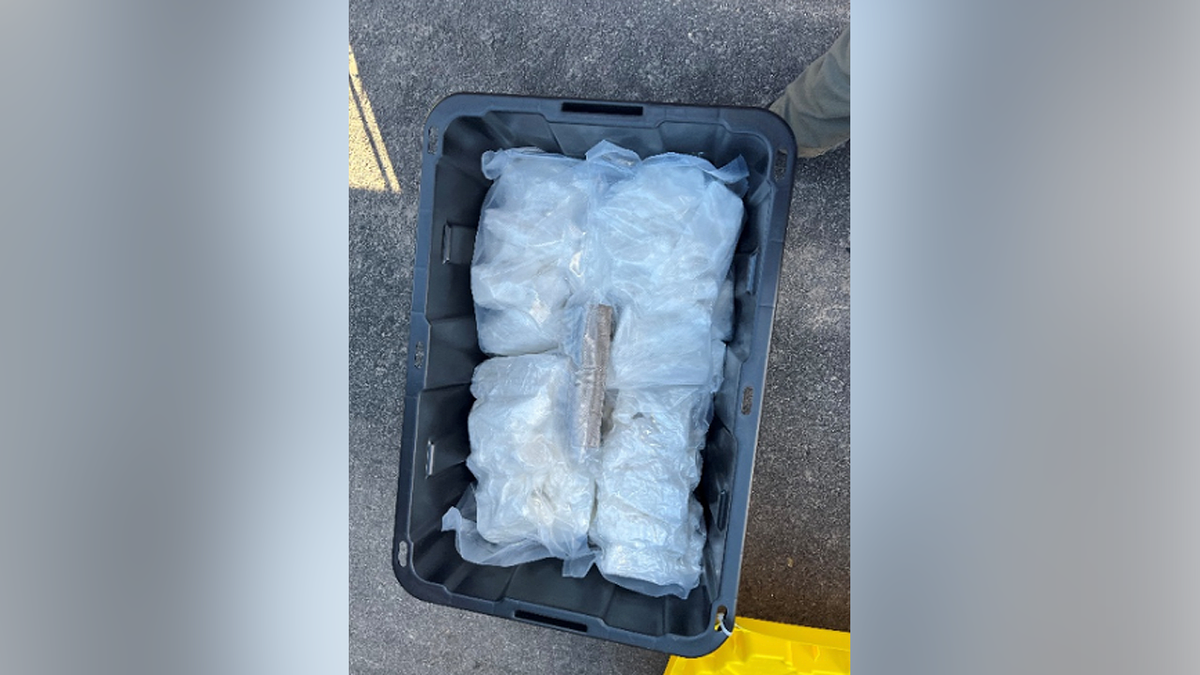 Open black storage tote containing clear plastic packages of suspected narcotics