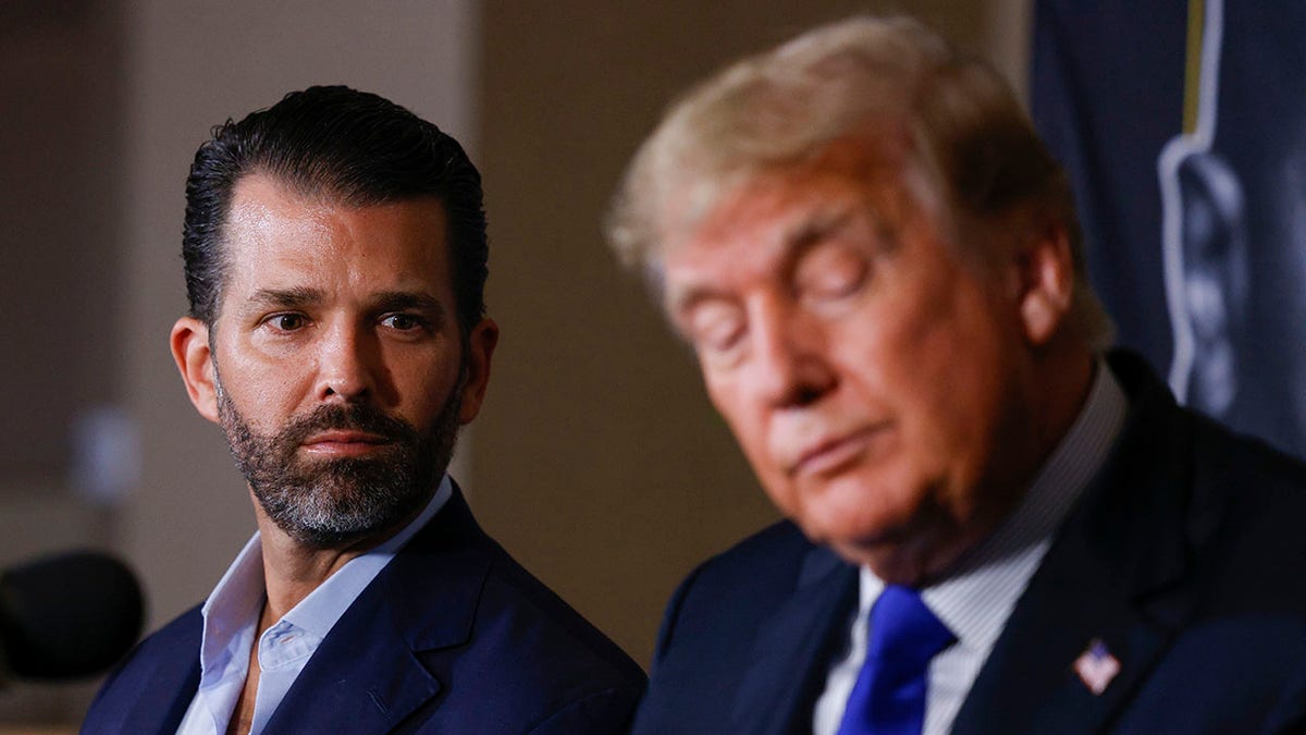 Donald Trump Jr. looks to his father, former President Donald Trump, on stage at a Florida event