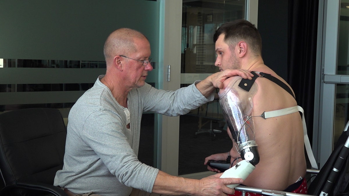 a doctor helps a man in a wheel chair with his new prosthetic arm
